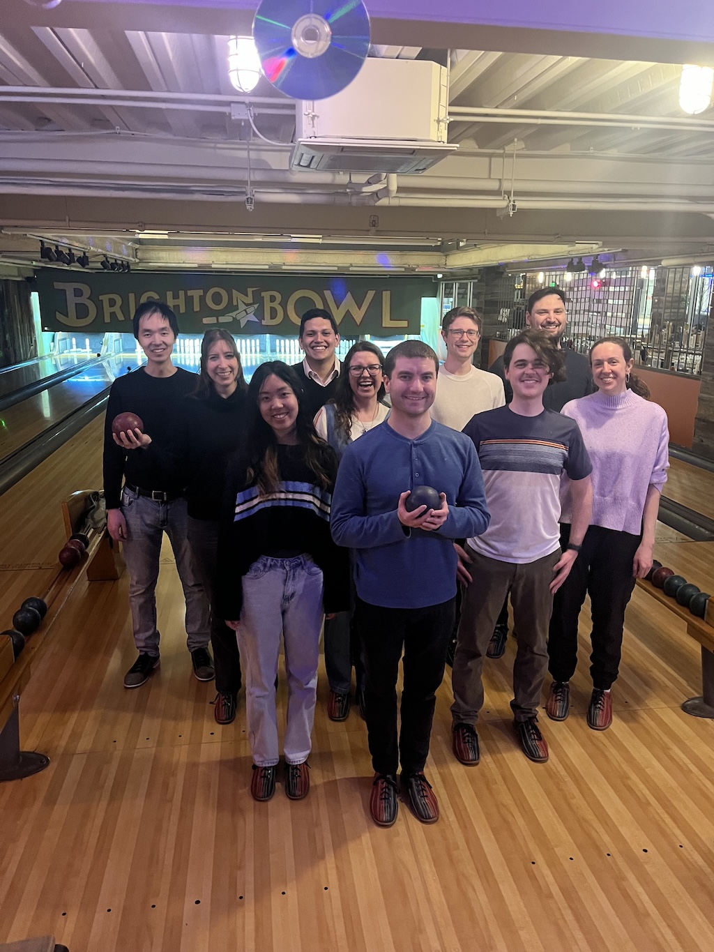 Ten lab members arranged like bowling pins taking a picture at a candlepin bowling alley.
